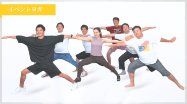 イベントヨガで参加者たちがインストラクターと一緒にワイドスタンスのポーズをとり、笑顔で身体を伸ばしている様子
