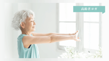 高齢の女性が明るい室内で腕を伸ばし、心地よさそうにヨガのポーズをとっている様子