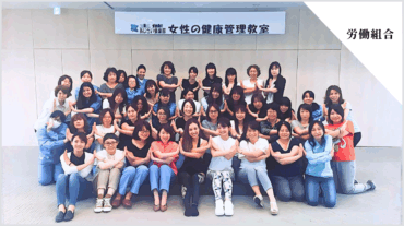労働組合の女性向け健康管理教室で、多くの参加者が腕をクロスさせたポーズで集合写真に写っている様子