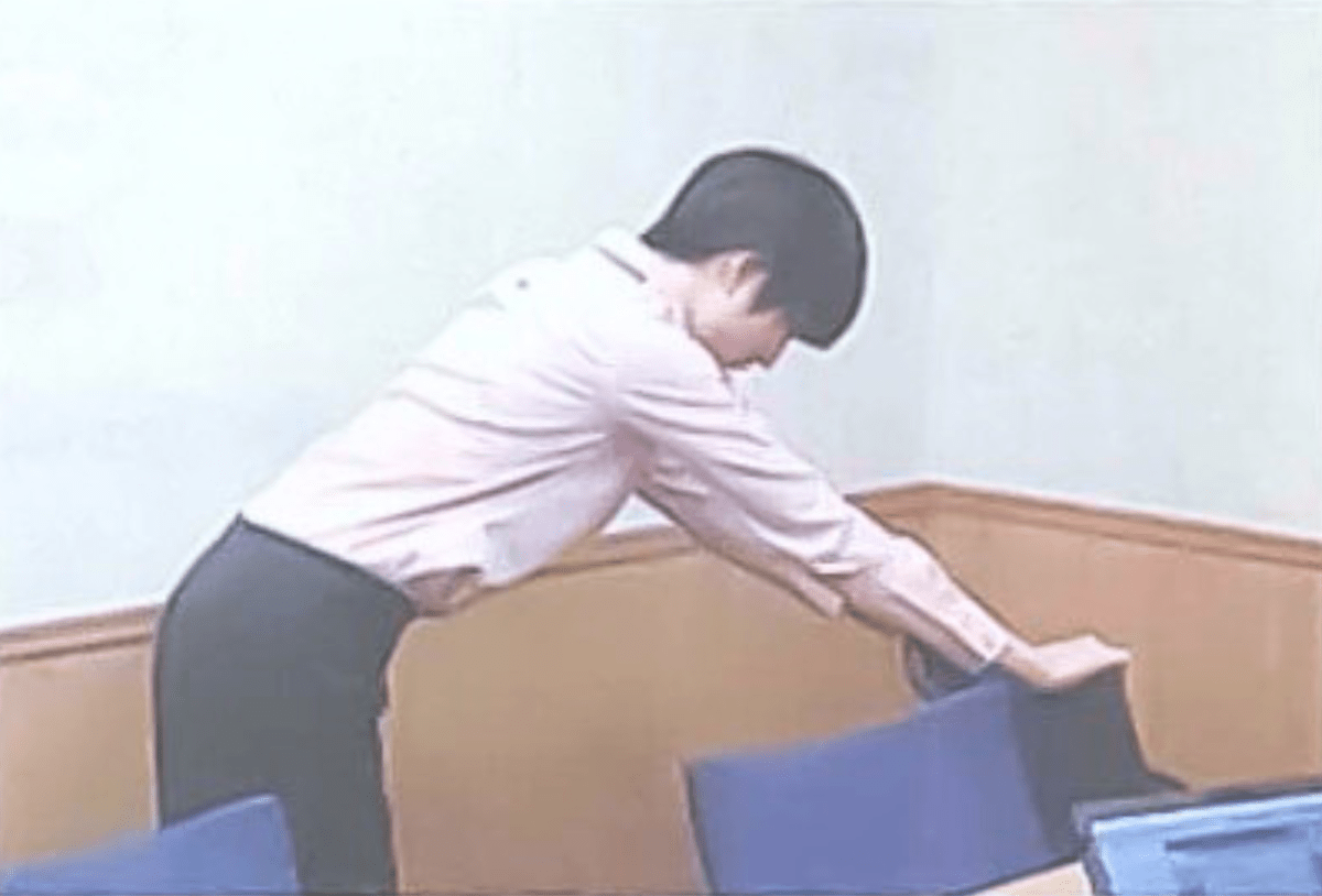 椅子の背もたれに手を置き、上半身を倒して背中を伸ばすようにストレッチを行っている様子