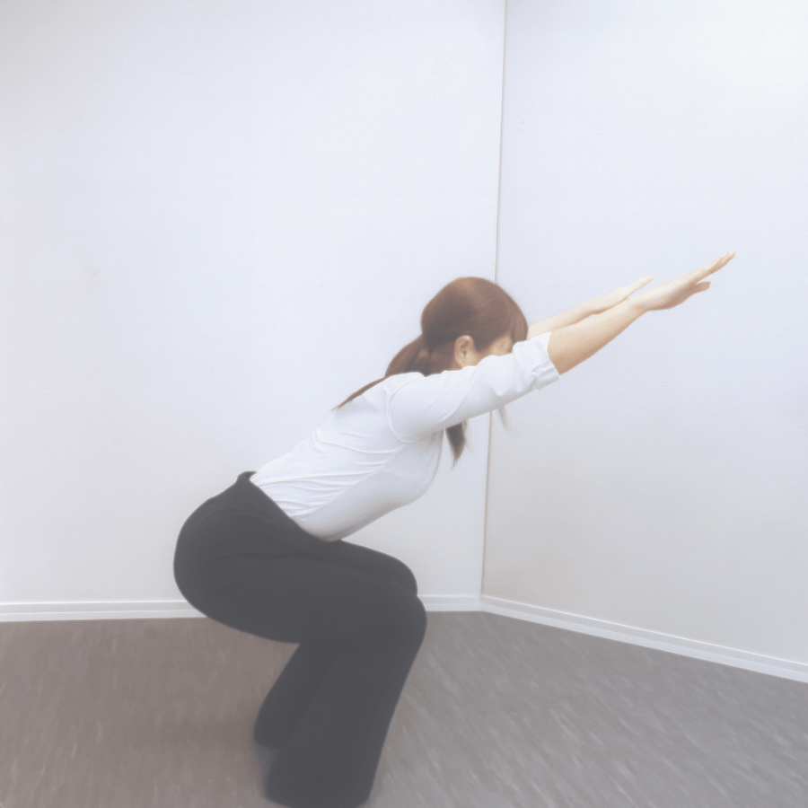 腕を前に伸ばしながら膝を曲げ、デスク周りでできる椅子のポーズ風のストレッチを行っている様子