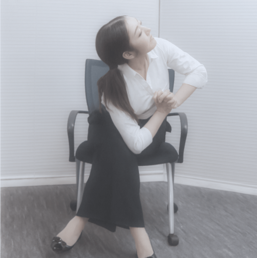椅子に座り片足を組んだ状態で、肘を膝の外側に当てて上半身をひねるストレッチを行っている様子