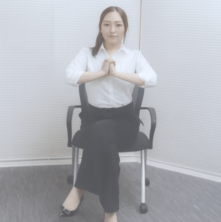 椅子に座り片足を組んだ姿勢で、胸の前で両手を合わせて姿勢を整えるストレッチの基本ポーズをとっている様子