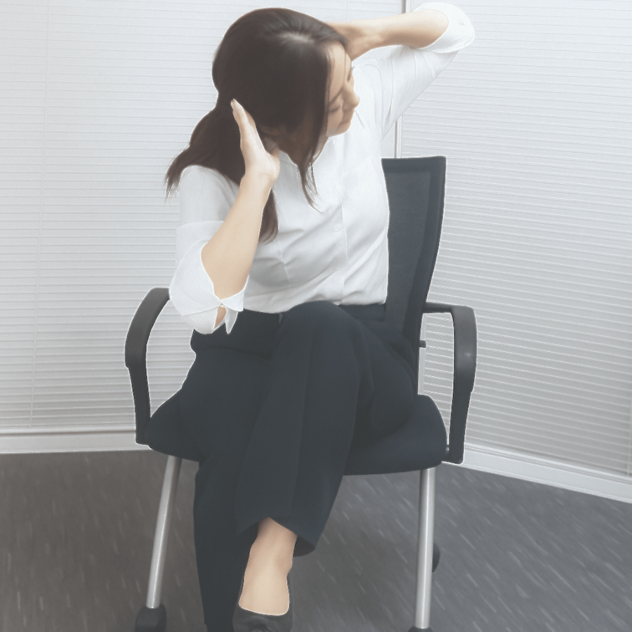 椅子に座り、片足を膝の上に乗せて体をひねり、腰まわりをほぐすストレッチを行っている様子