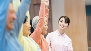 見守りスタッフのもとで腕を上げる体操を行う高齢者