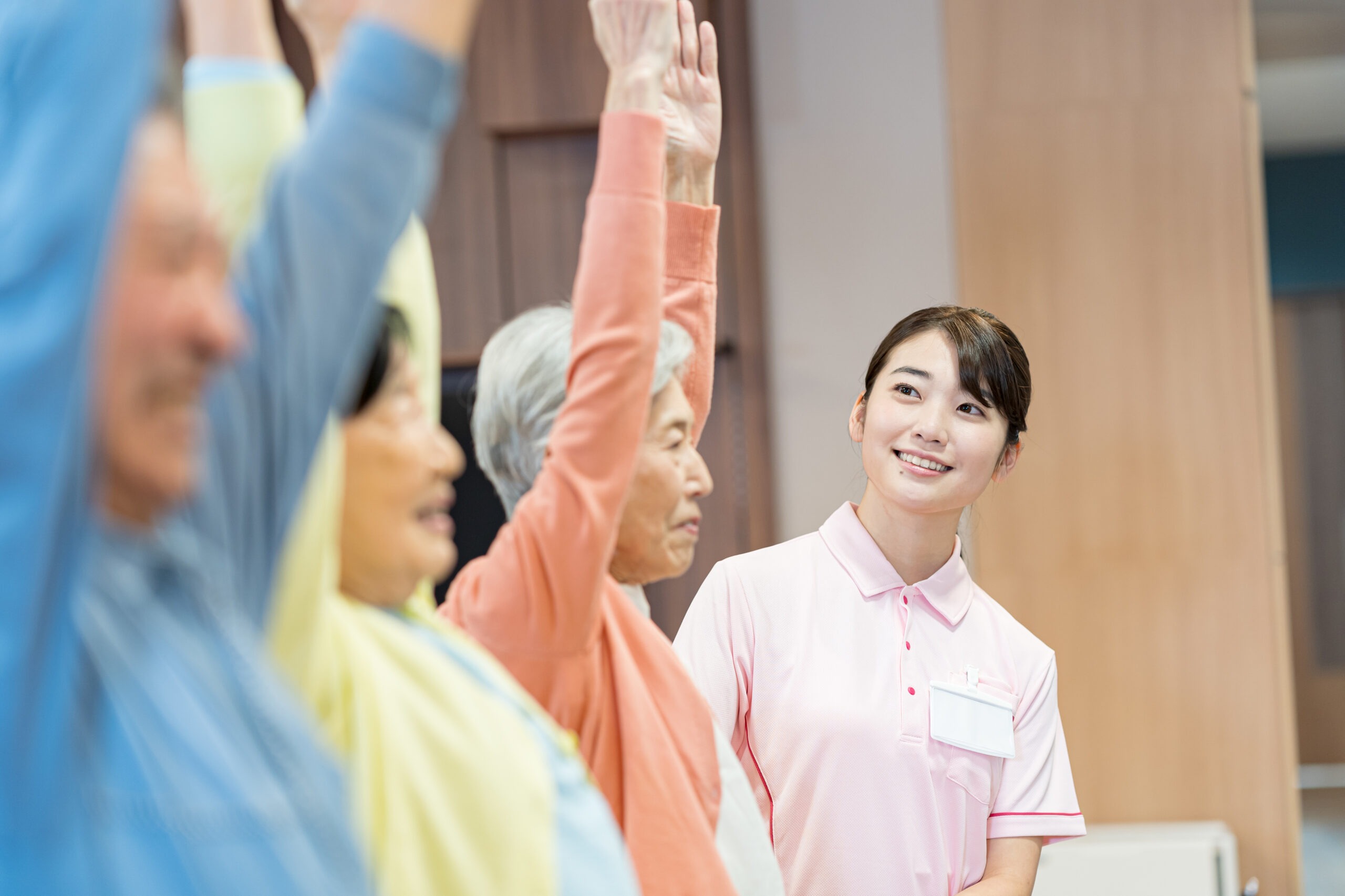 見守りスタッフのもとで腕を上げる体操を行う高齢者