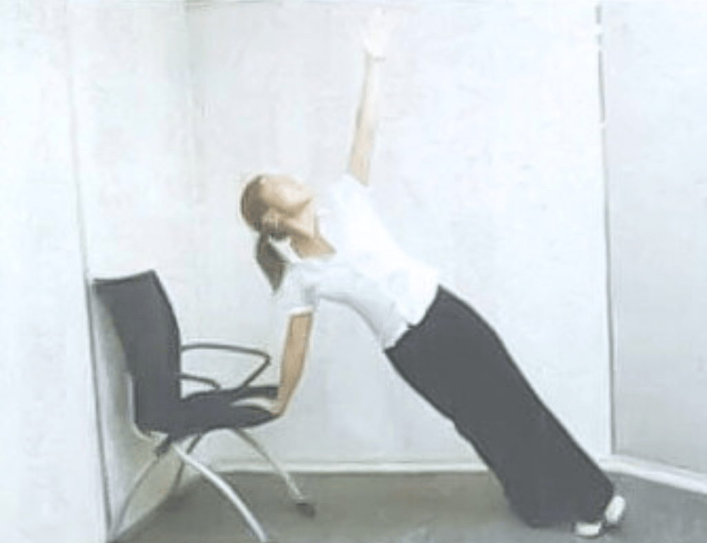 椅子に片手を置きながら体を傾け、反対の腕を天井へ伸ばして胸を開くように行うヨガのアレンジポーズ